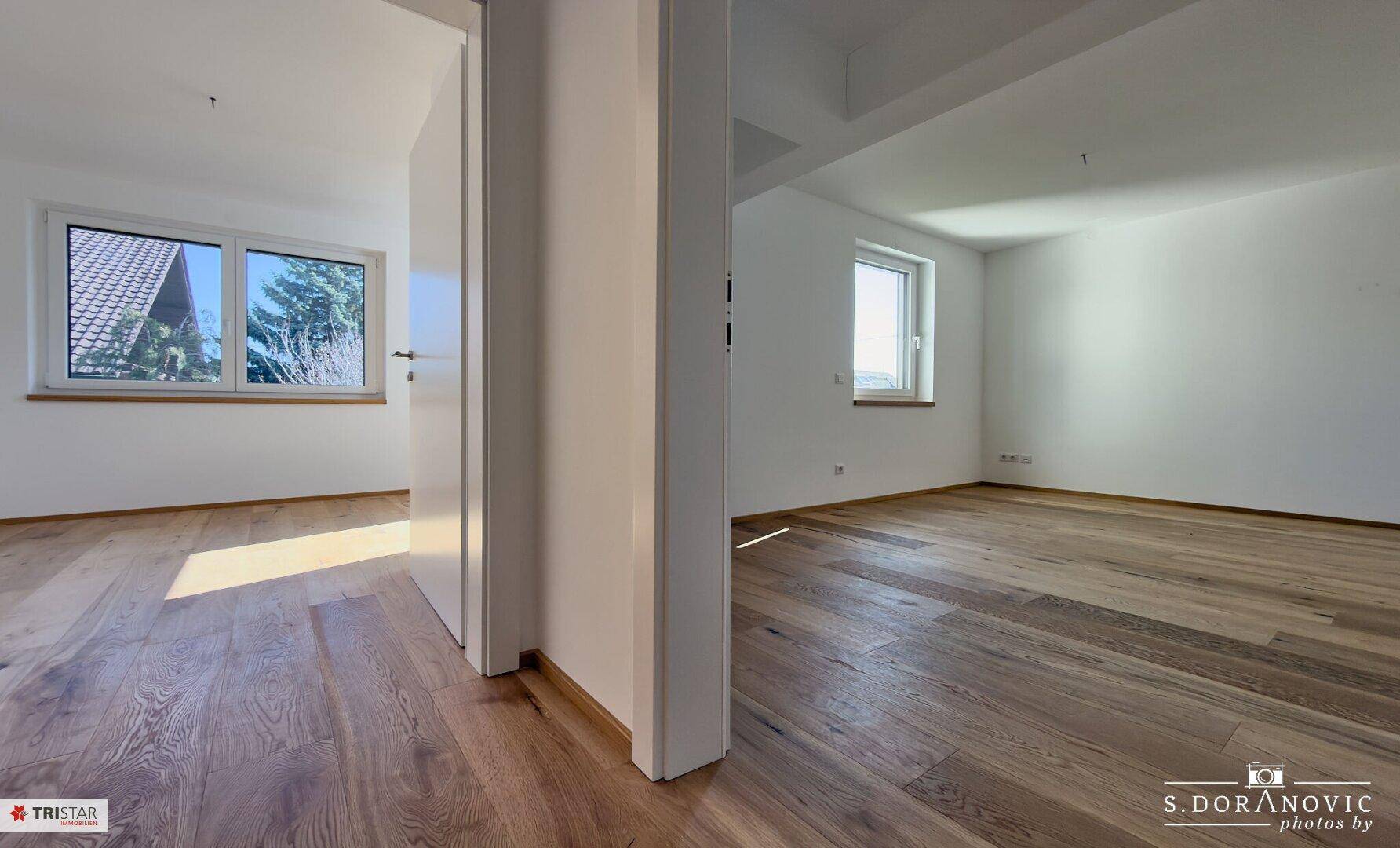 Helle, leere Räume mit Holzboden und Fenstern mit Blick ins Grüne.