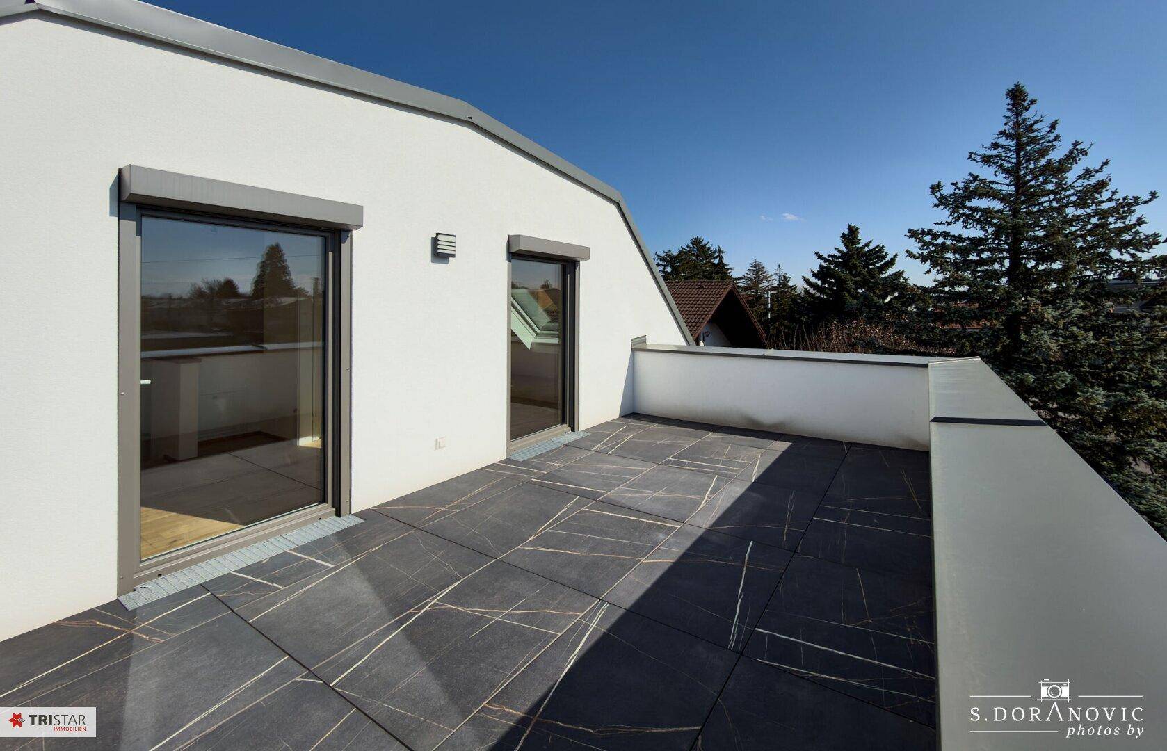 Geräumige Dachterrasse mit dunklen Fliesen und weitem Blick unter blauem Himmel.