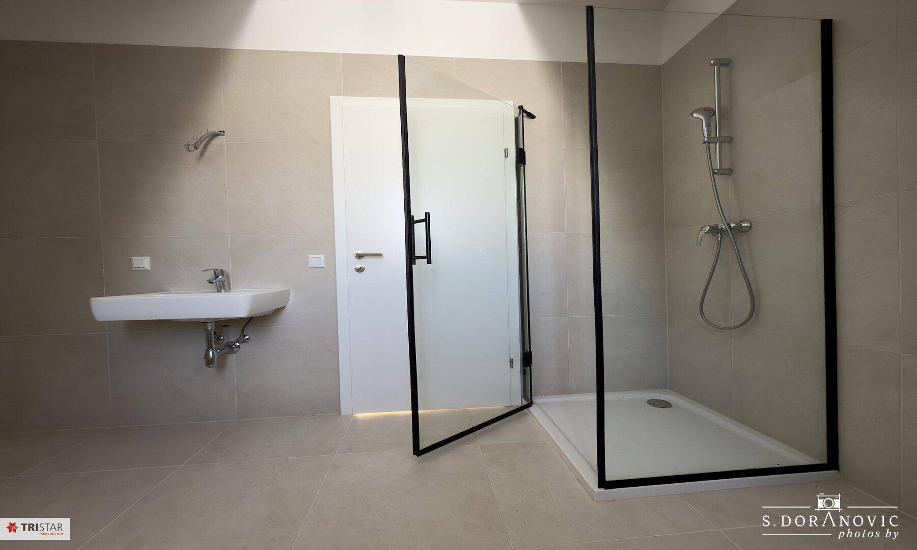 Modernes Badezimmer mit Duschkabine, Einzelwaschbecken und hellgrauen Fliesen.