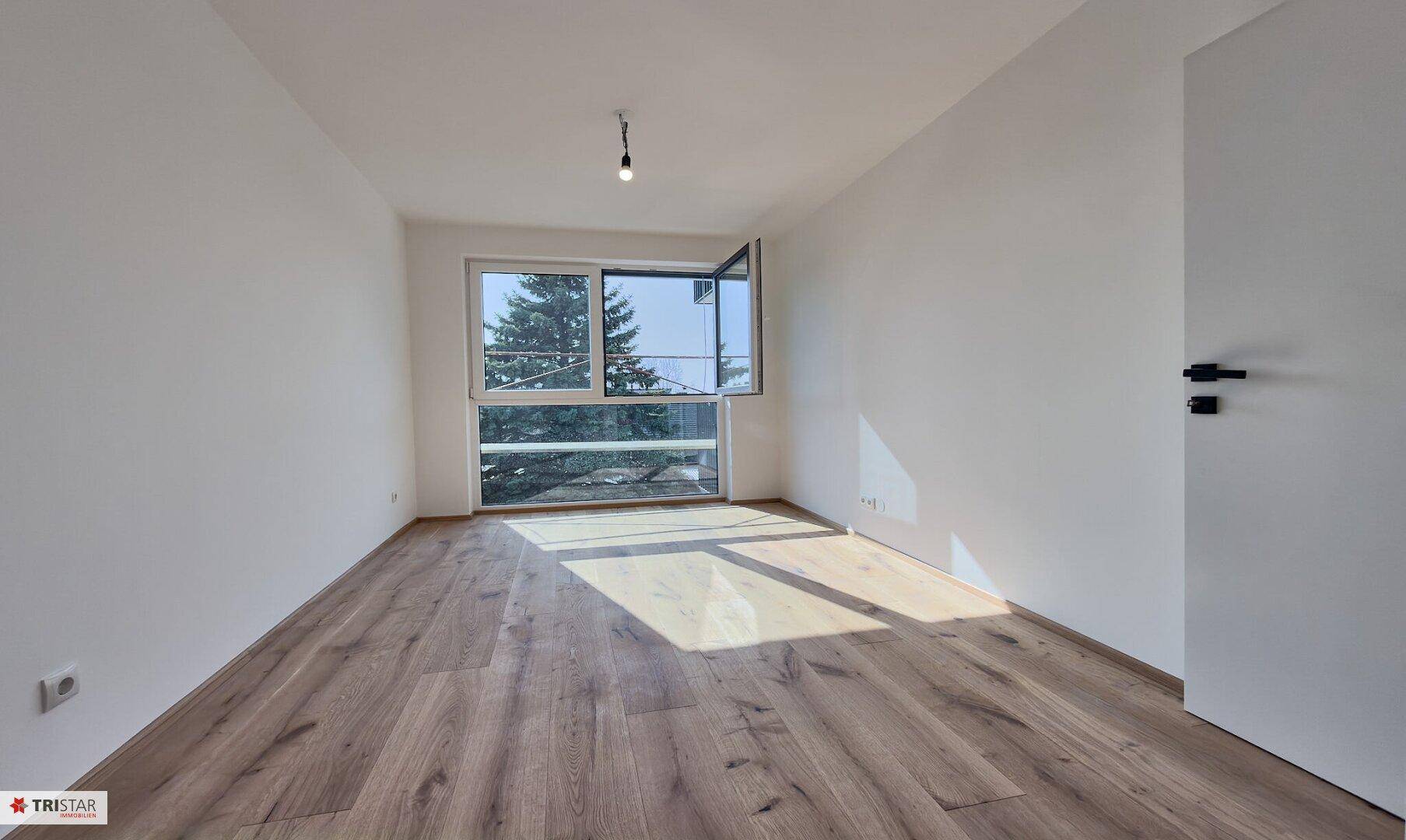 Helles Schlafzimmer mit Holzboden und großem Fenster, das eine angenehme Atmosphäre schafft.