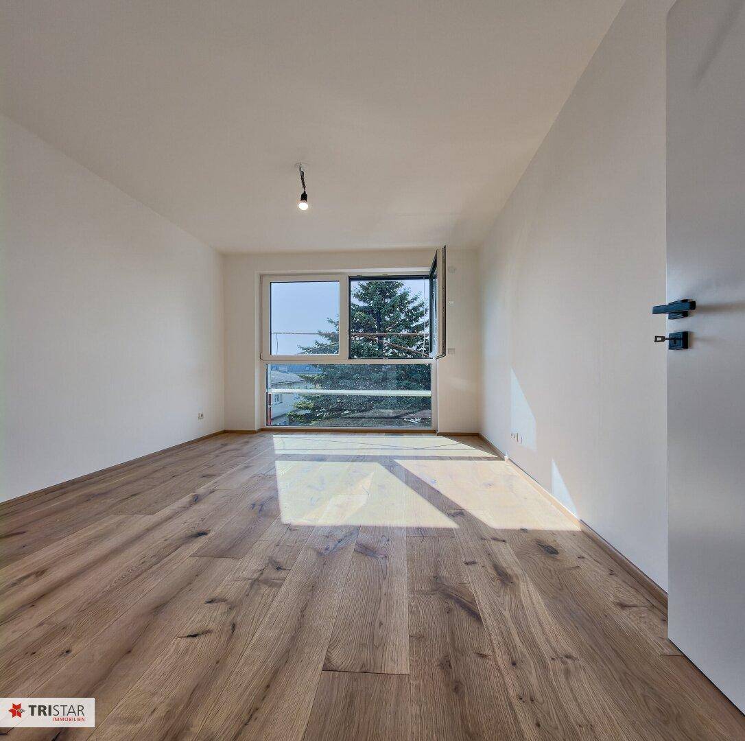 Helles Schlafzimmer mit Holzboden und großem Fenster, das viel Tageslicht hereinlässt.