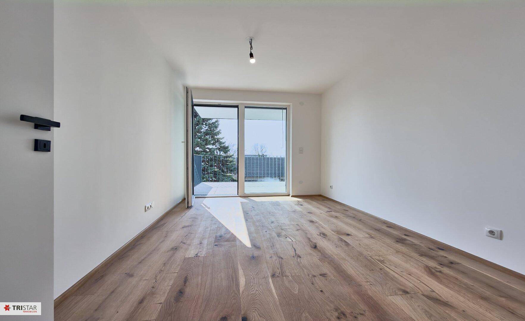 Geräumiges Schlafzimmer mit Holzboden und Zugang zu einem sonnigen Balkon.