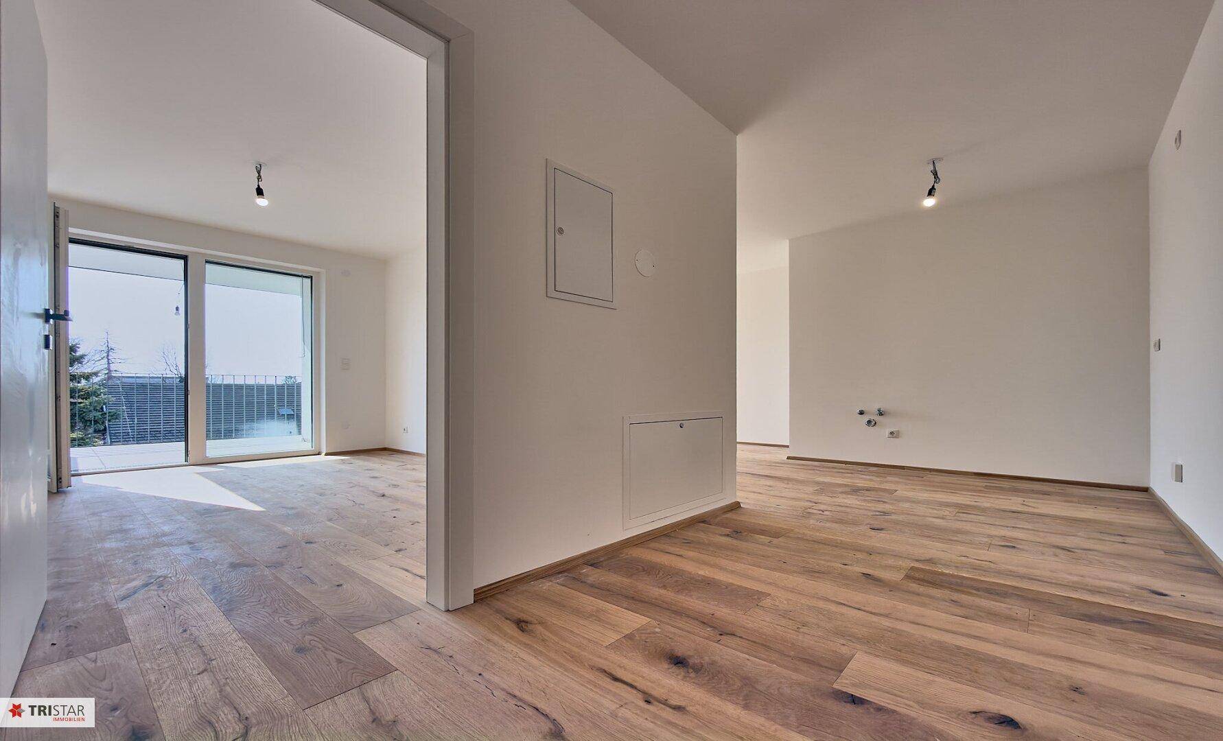 Geräumiger, heller Wohnbereich mit Holzboden und Blick auf den Balkon und weitere Räume.