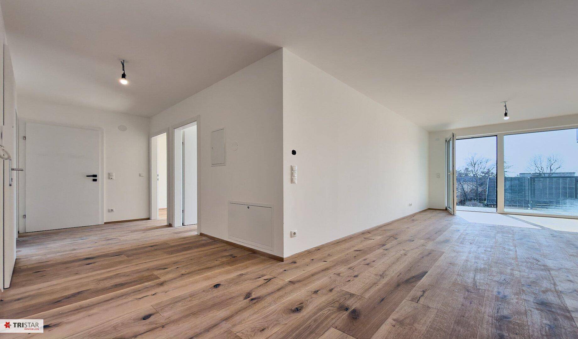Heller, leerer Wohnbereich mit neuem Holzboden und Zugang zu einem sonnigen Außenbereich.
