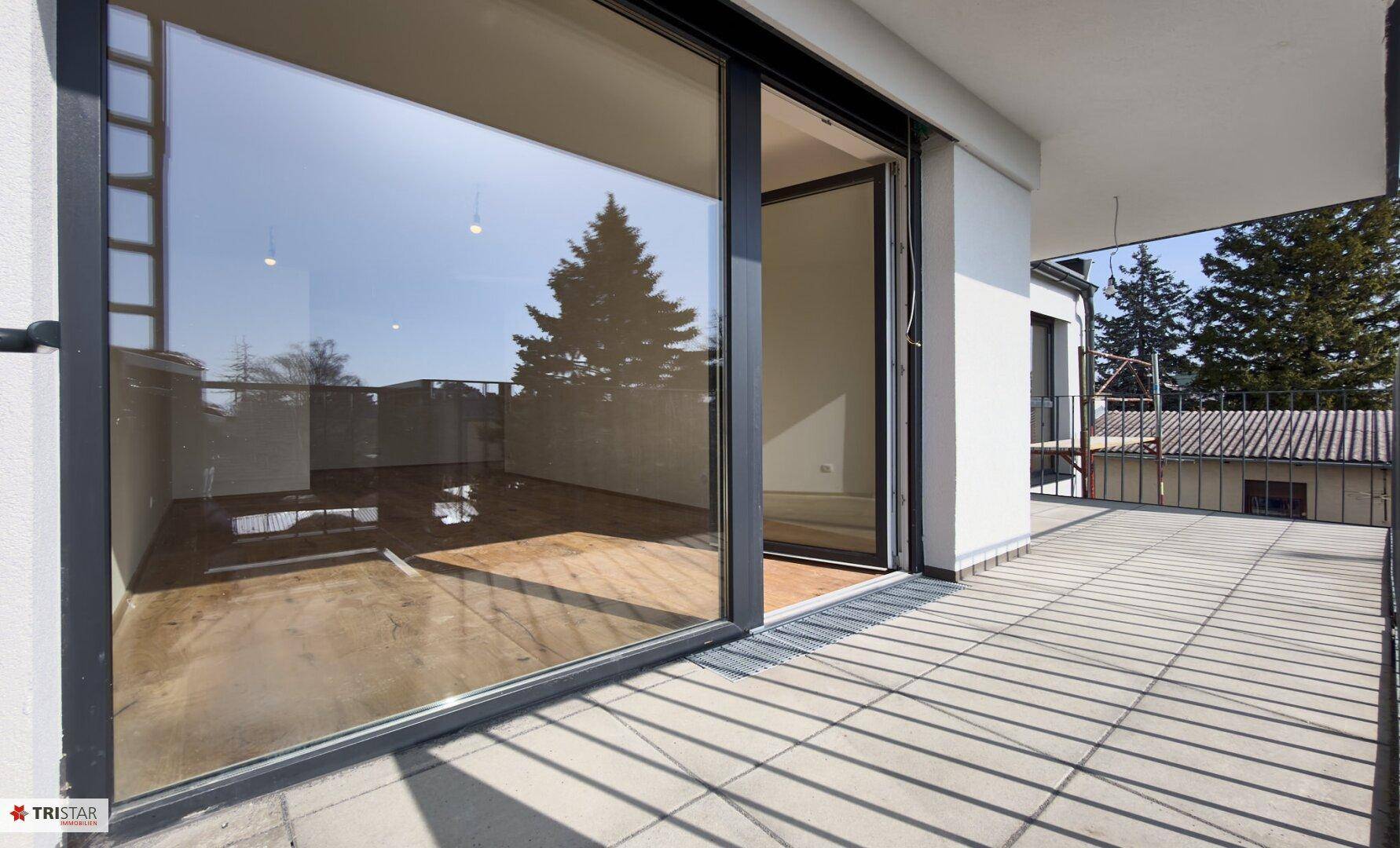 Balkon mit Fliesenboden und Blick in den hellen Innenraum durch große Schiebetüren.