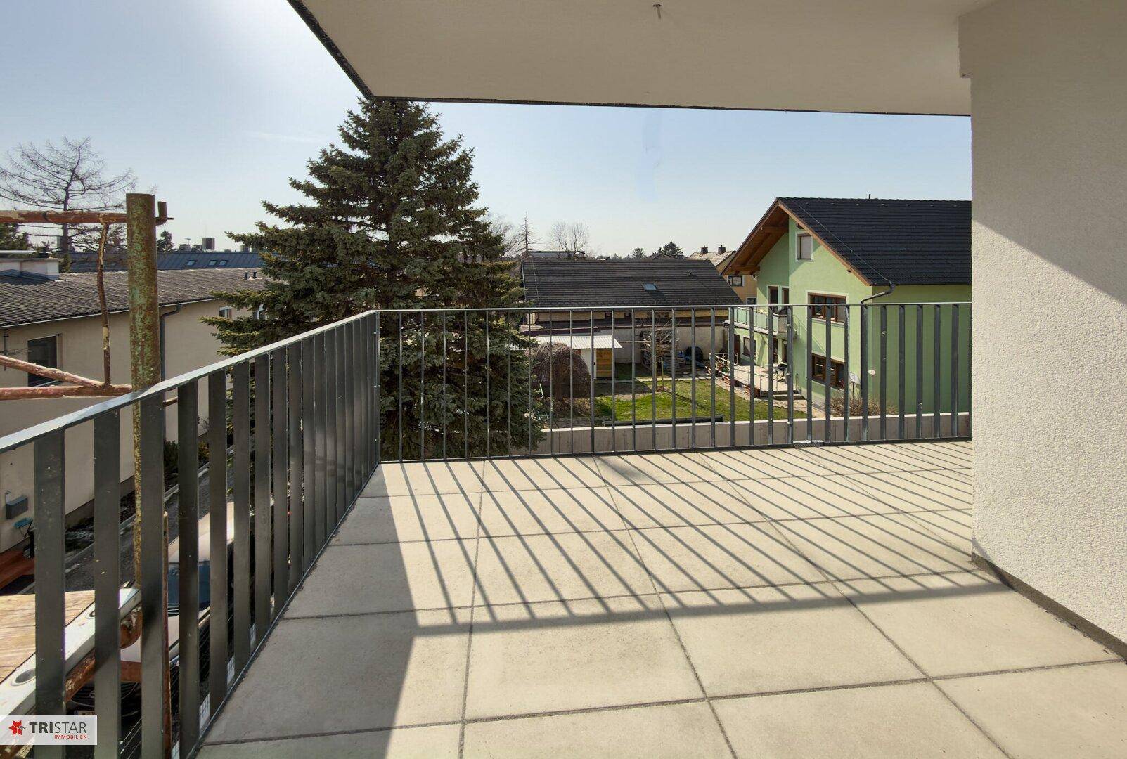 Sonniger Balkon mit Fliesenboden und Blick auf die umliegenden Häuser und Bäume.