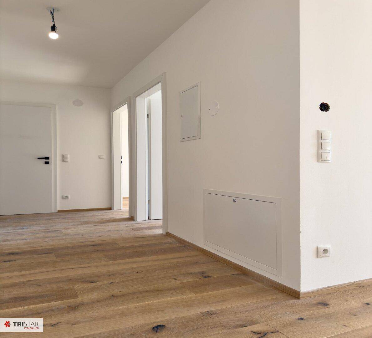 Heller Flur mit Holzboden und weißen Wänden, der zu weiteren Räumen führt.
