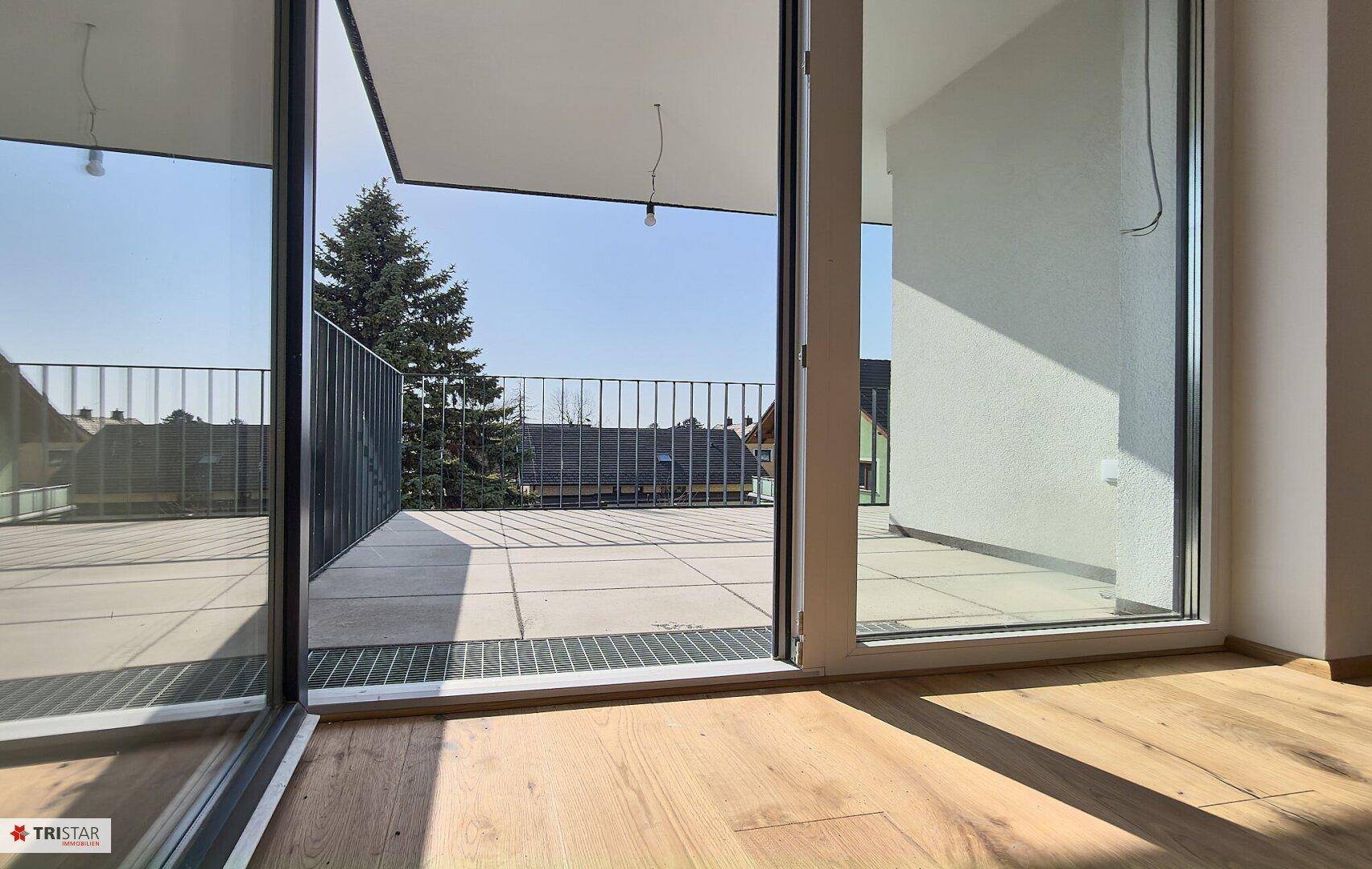 Heller Innenraum mit Holzplankenboden und direktem Zugang zu einem großen, gefliesten Balkon.