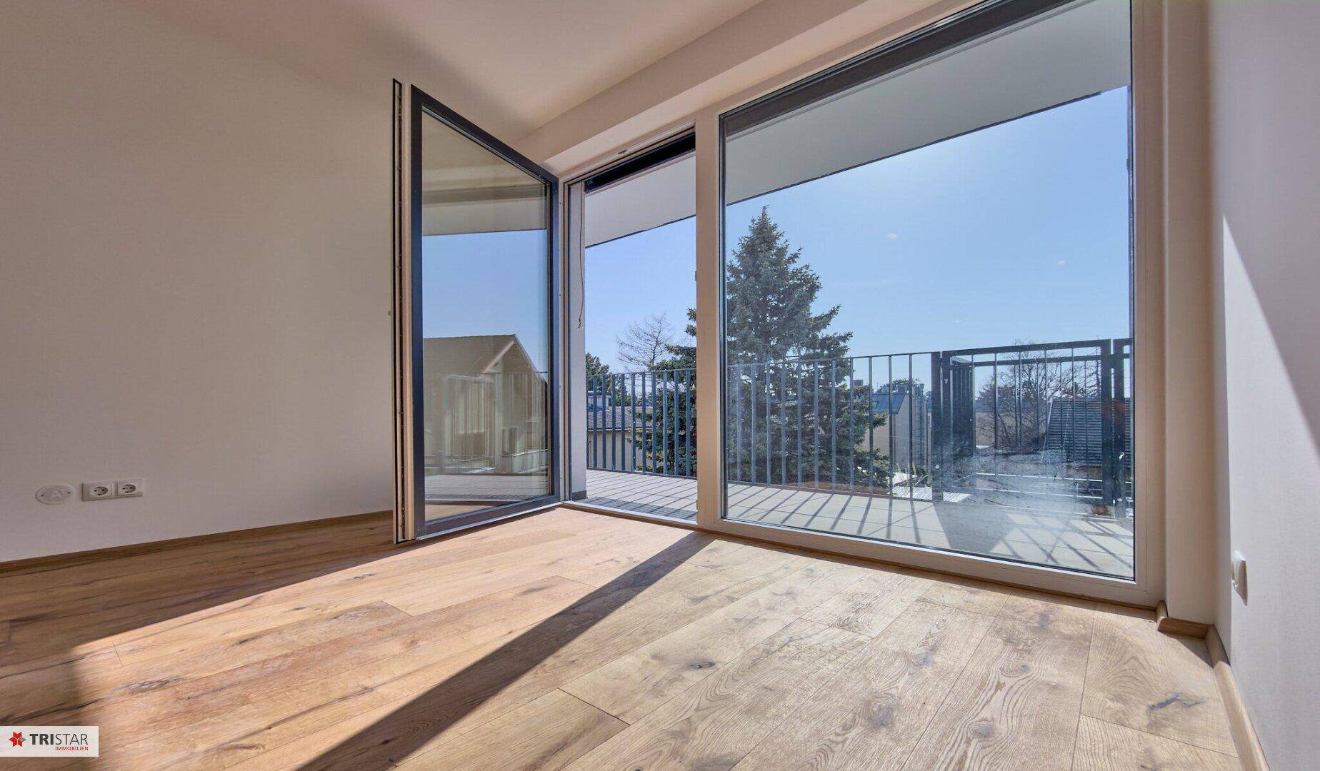 Große Fensterfront mit Zugang zu einem Balkon, bietet einen Blick auf Bäume und die Umgebung.