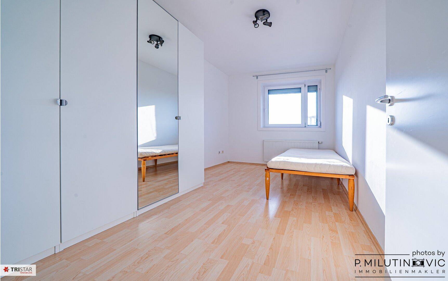 Schlafzimmer mit Laminatboden, Einzelbett und einem großen Spiegelschrank.
