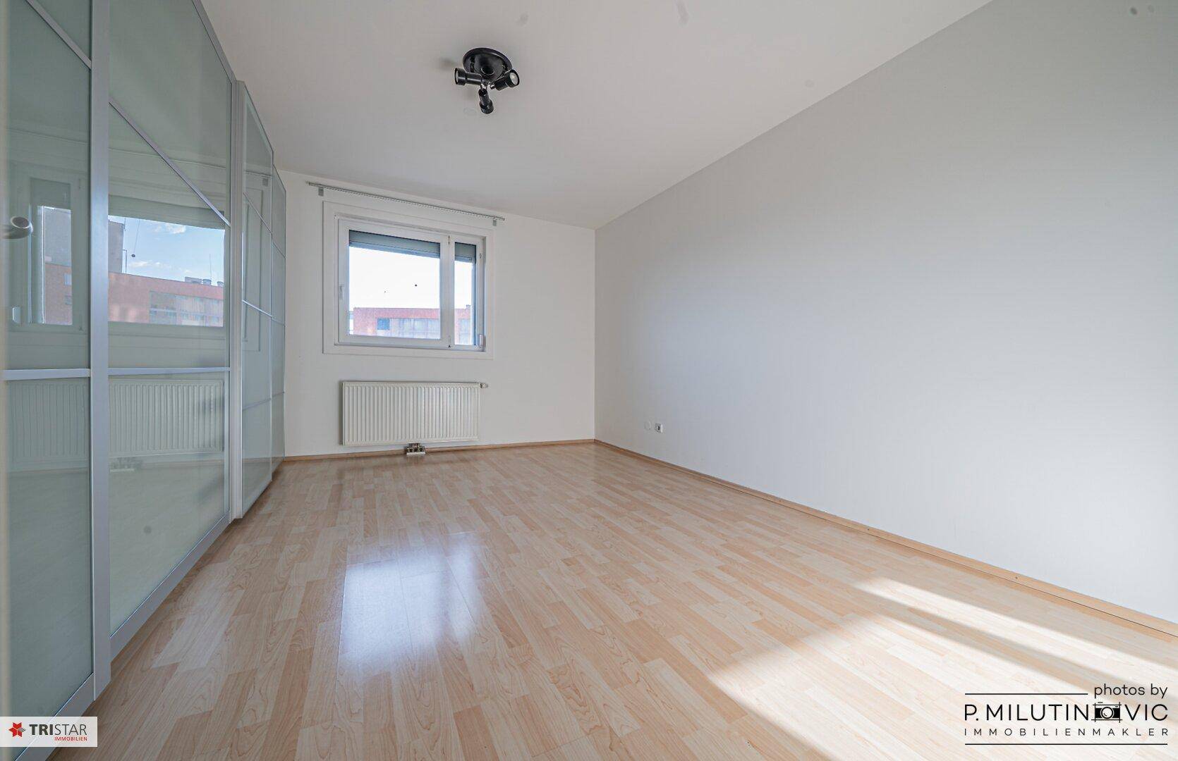 Helles Schlafzimmer mit Laminatboden, großem Fenster und einem modernen Kleiderschrank.