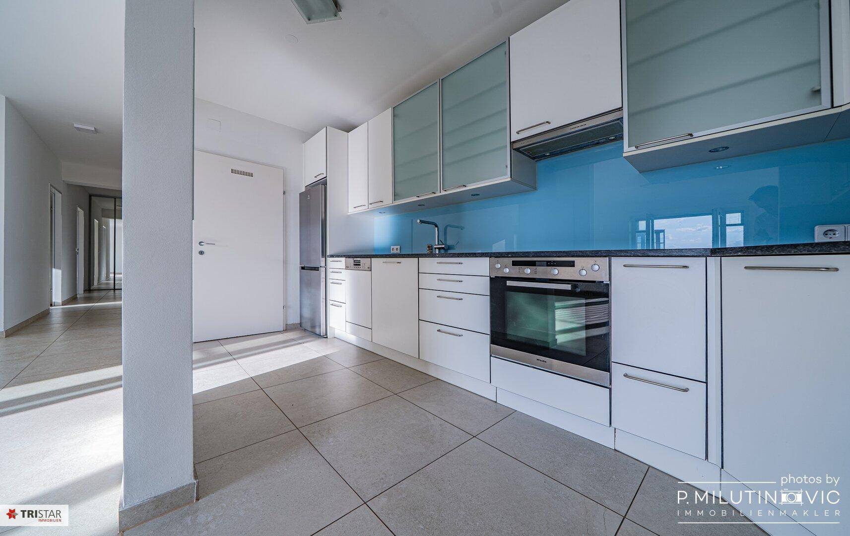 Moderne Einbauküche mit weißen Schränken, blauer Rückwand und integrierten Geräten.