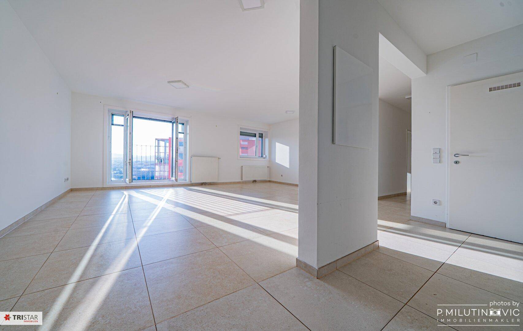 Geräumiger, heller Wohnbereich mit Fliesenboden und Zugang zu einem französischen Balkon.