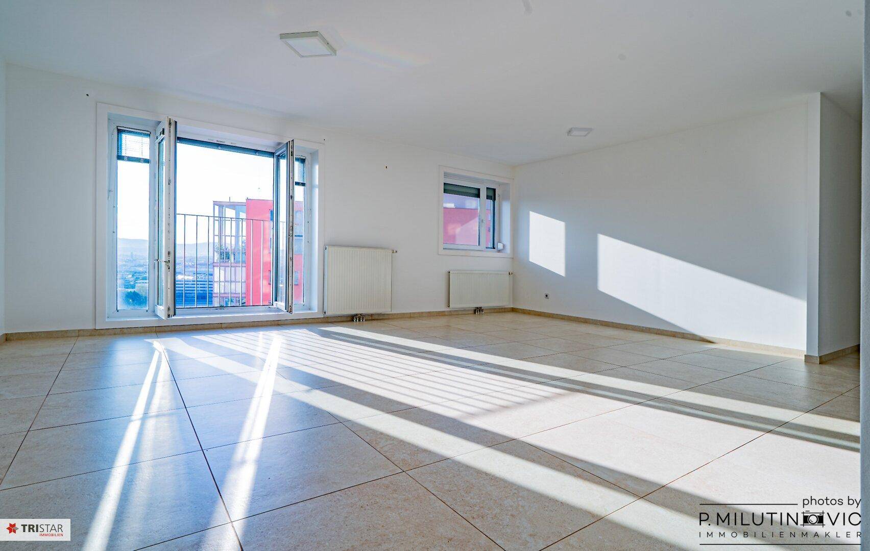 Lichtdurchfluteter, leerer Raum mit Fliesenboden und Zugang zu einem französischen Balkon.