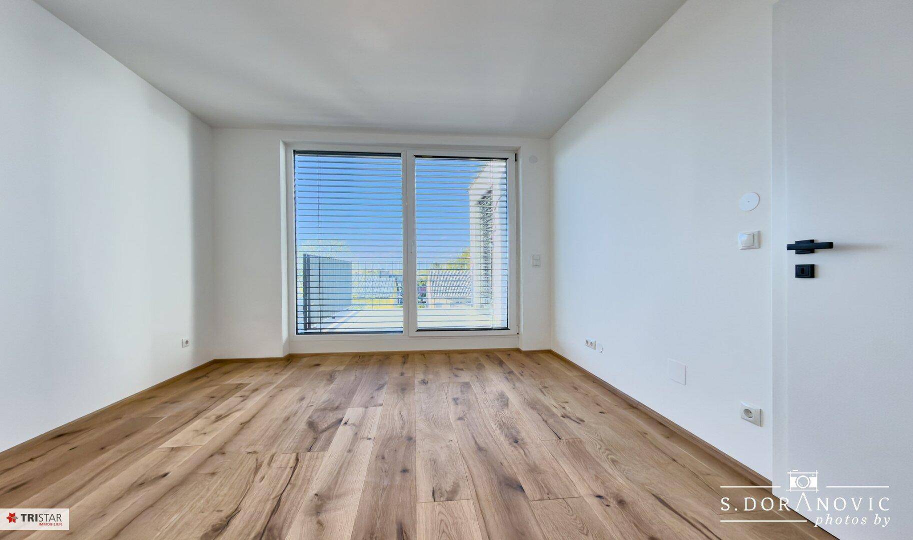 Helles Schlafzimmer mit Holzboden und großem Fenster, das viel Tageslicht bietet.