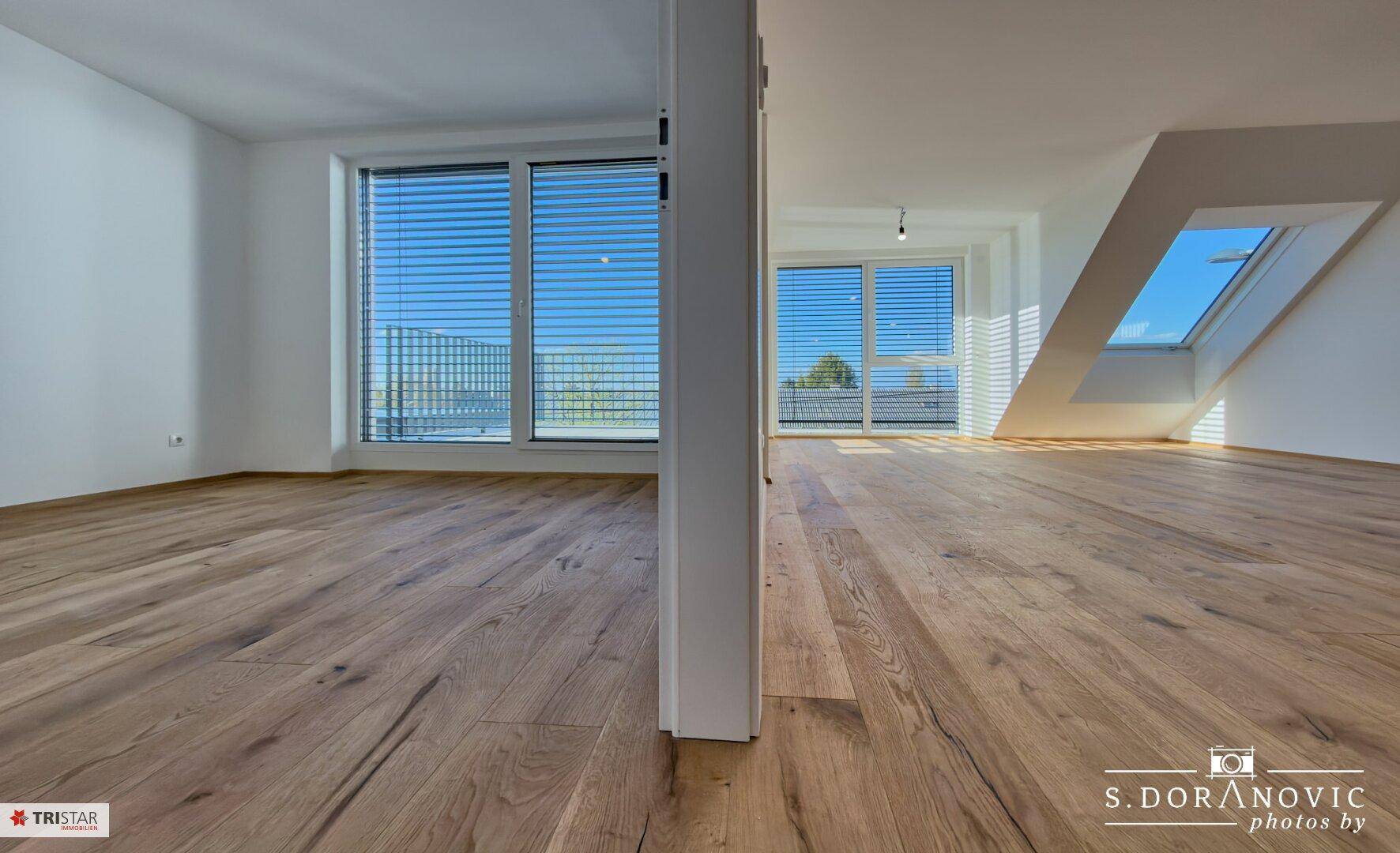 Geräumiger Wohnbereich mit Holzboden, Dachschrägen und großen Fenstern für viel Licht.