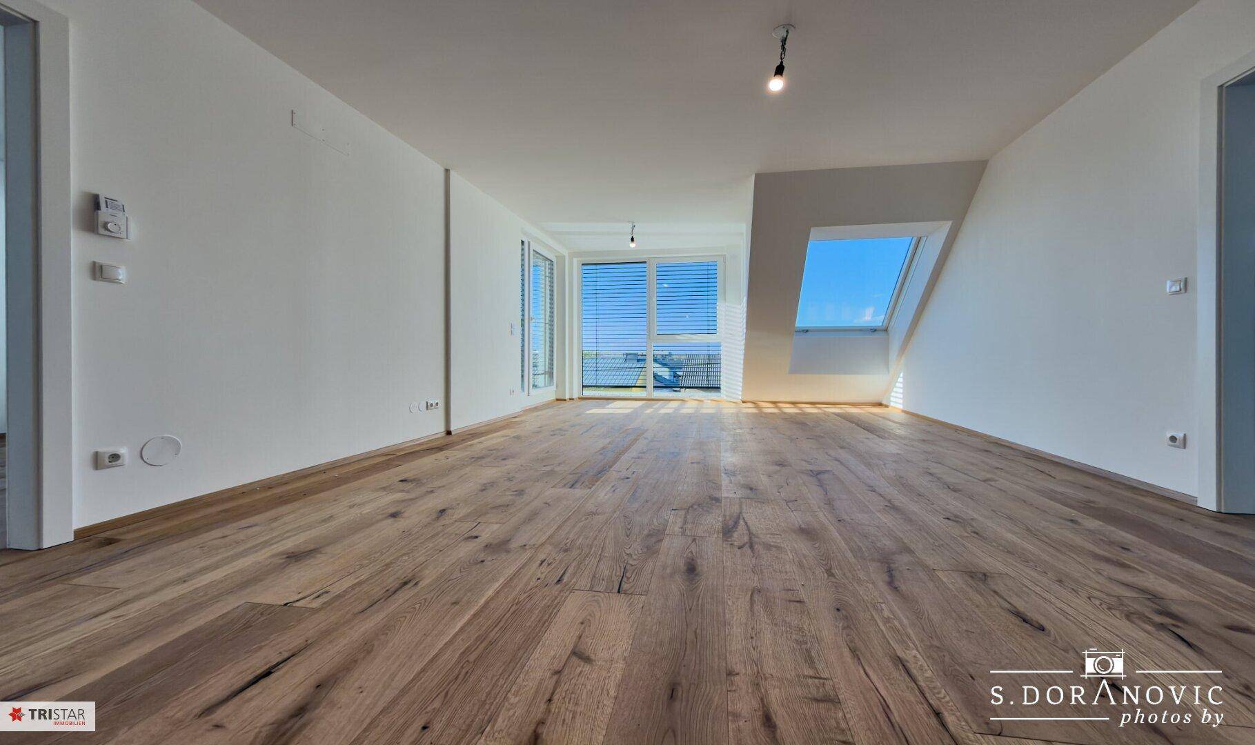 Weitläufiger Wohnbereich mit Holzboden, Dachschrägen und großen Fenstern für eine helle Atmosphäre.