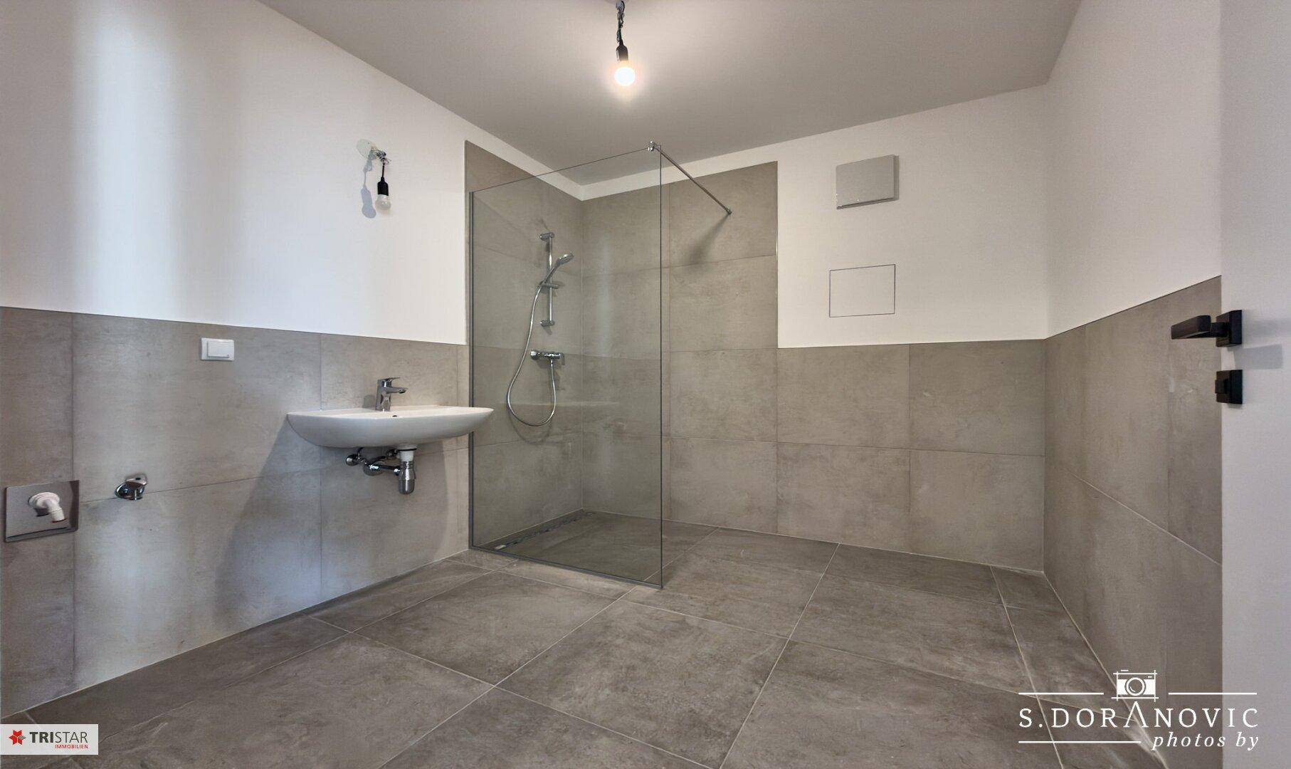 Modernes Badezimmer mit grauen Fliesen, Einzelwaschbecken und einer begehbaren Dusche.