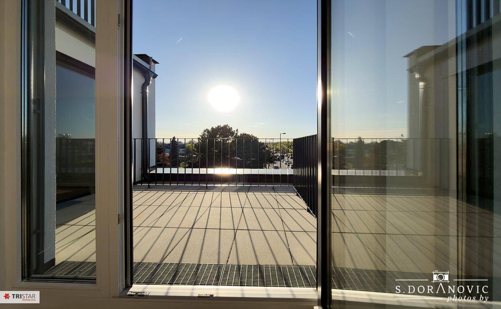 Heller Raum mit Zugang zu einer Terrasse und Blick auf die Umgebung bei Sonnenschein.
