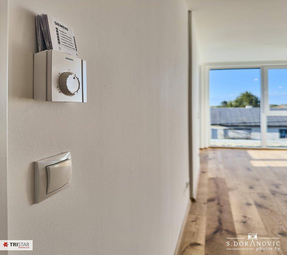 Detailaufnahme eines Siemens-Thermostats und Lichtschalters an einer weißen Wand.