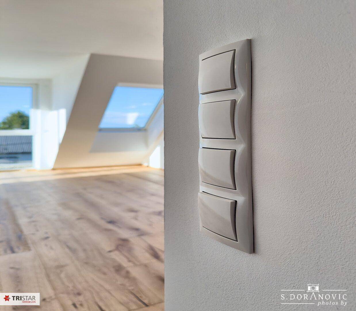 Nahaufnahme eines modernen Lichtschalters an einer weißen Wand in einem hellen Raum.