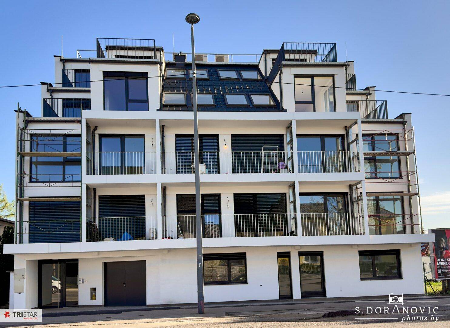 Vorderansicht eines modernen Apartmentgebäudes mit Balkonen und großen Fenstern zur Straße hin.