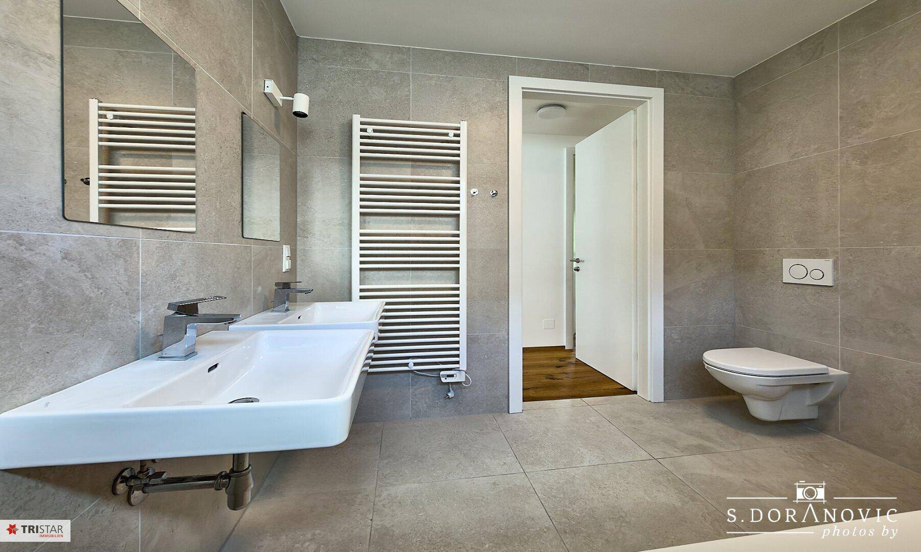 Modernes Badezimmer mit doppelten Waschbecken, Wand-WC und beheiztem Handtuchhalter.