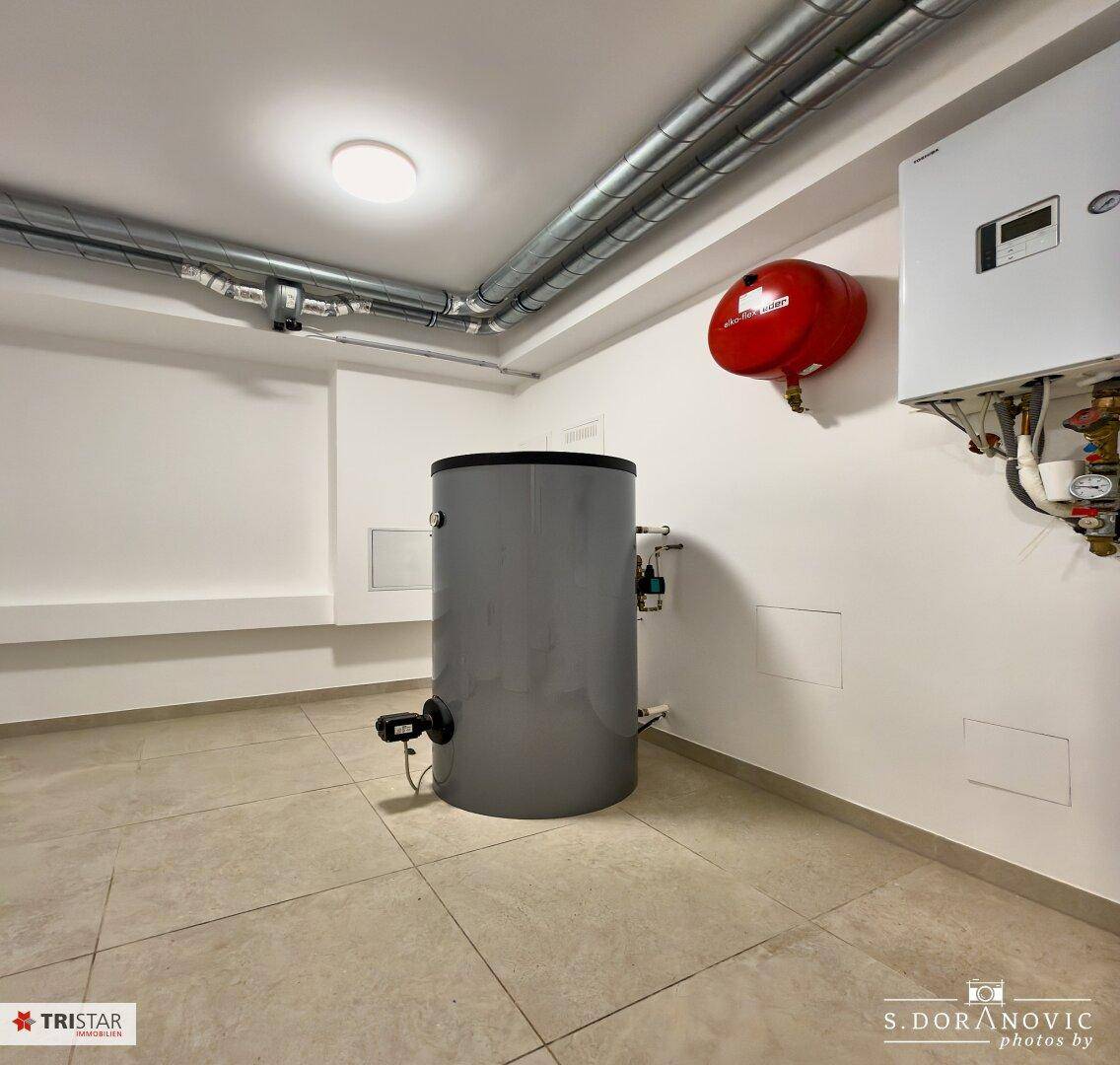 Technikraum mit Fliesenboden, Warmwasserspeicher und Heizungsanlage.