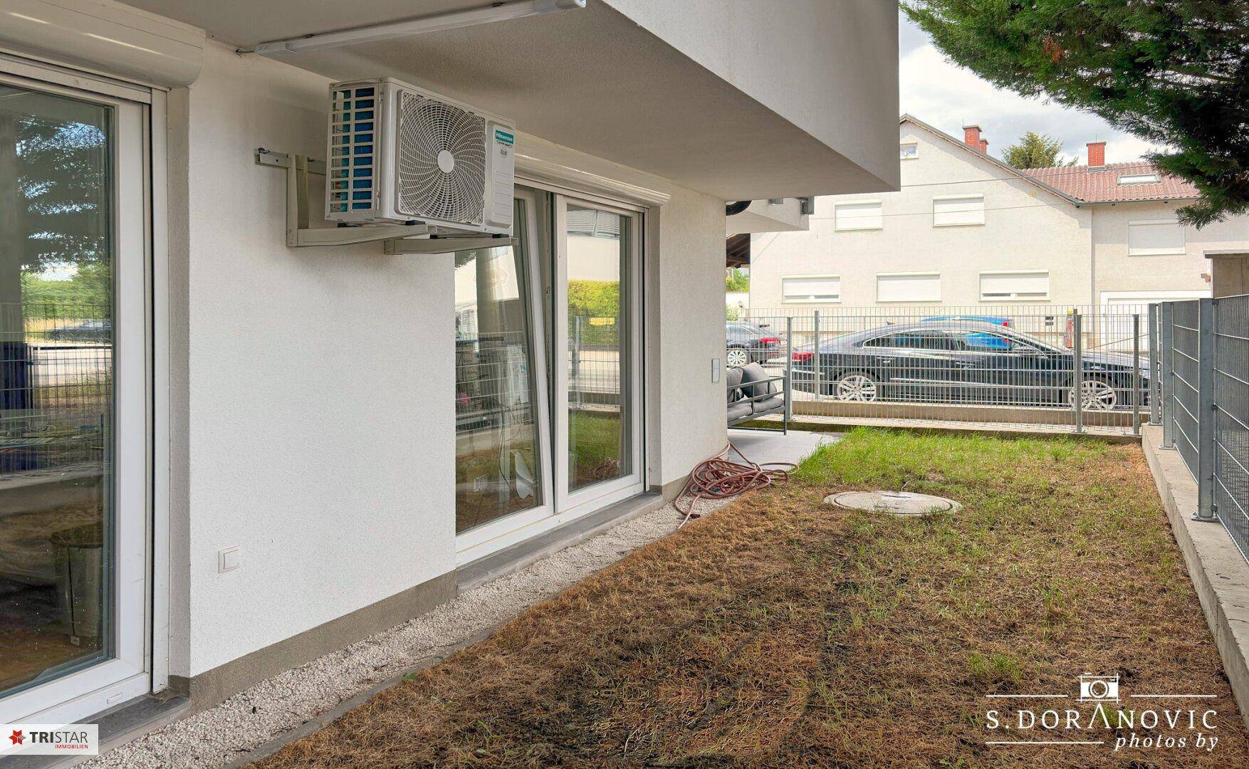 Gartenbereich mit Rasen und Klimaanlage an der Außenwand des Gebäudes.