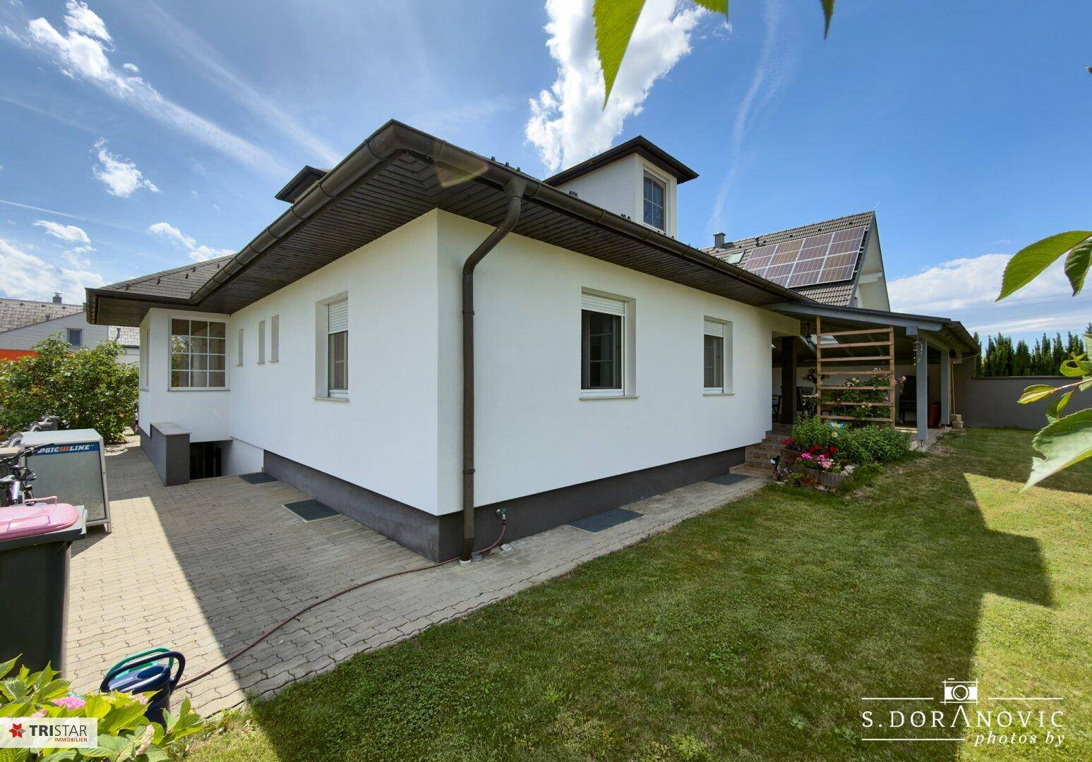 Seitenansicht des Hauses mit Garten, gepflastertem Bereich und überdachtem Sitzplatz.