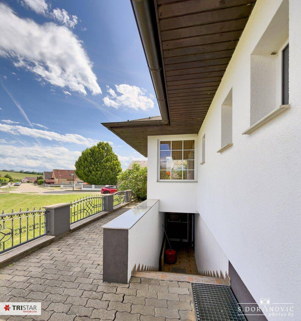 Seitlicher Zugang zum Haus mit Treppe zum Keller und Blick auf die ländliche Umgebung.