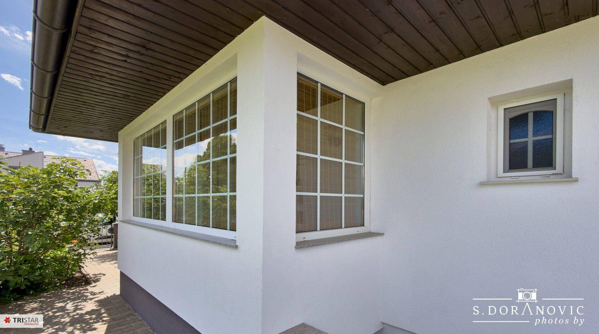 Detailansicht der weißen Fassade mit großen Sprossenfenstern und Holzdachüberstand.