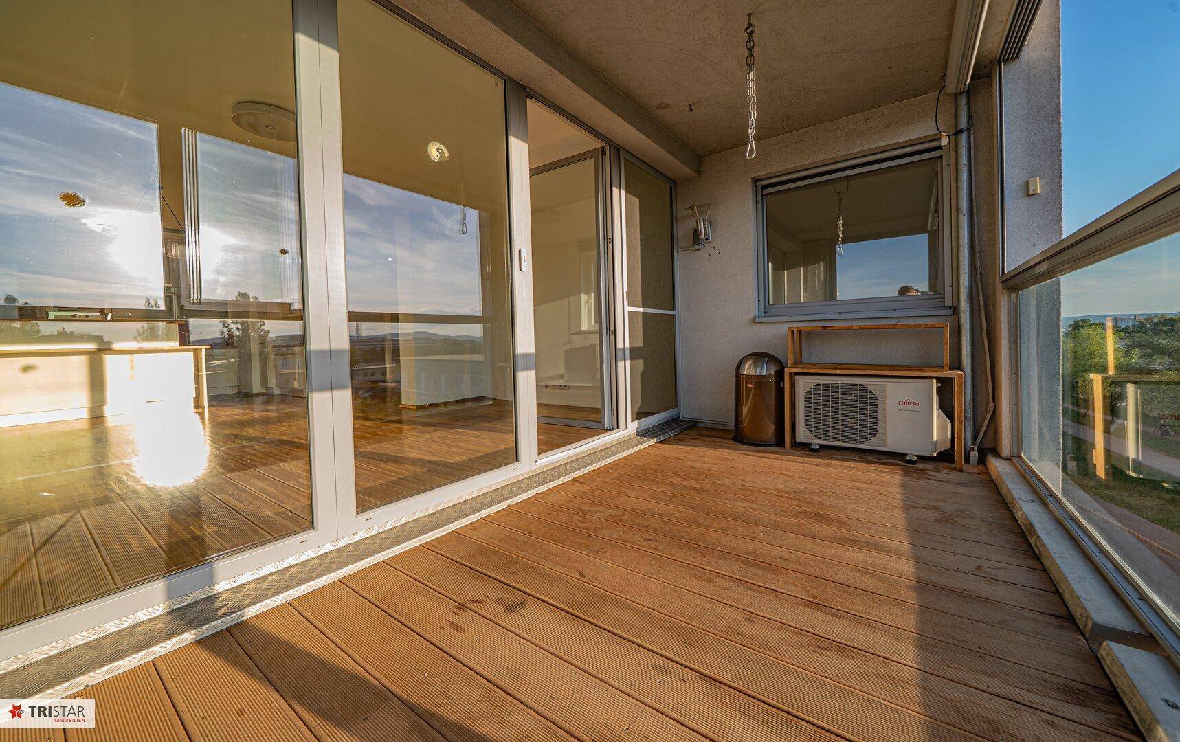 Geräumiger Balkon mit Holzboden und Klimaanlage, ideal für Entspannung im Freien.