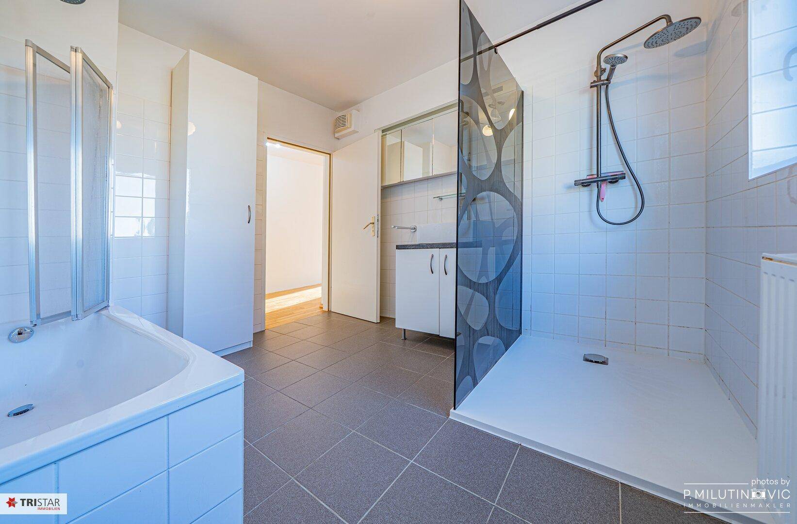 Modernes Badezimmer mit Badewanne, ebenerdiger Dusche und grauen Fliesen.
