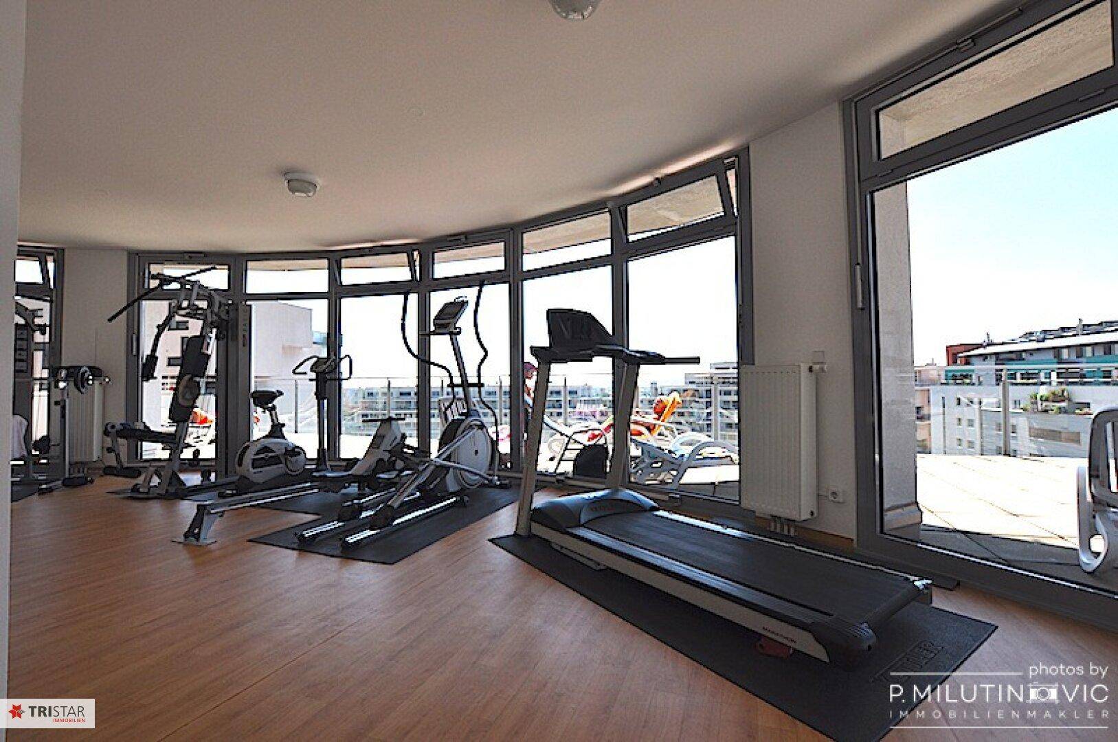 Fitnessraum mit verschiedenen Trainingsgeräten und Panoramablick durch große Fenster.