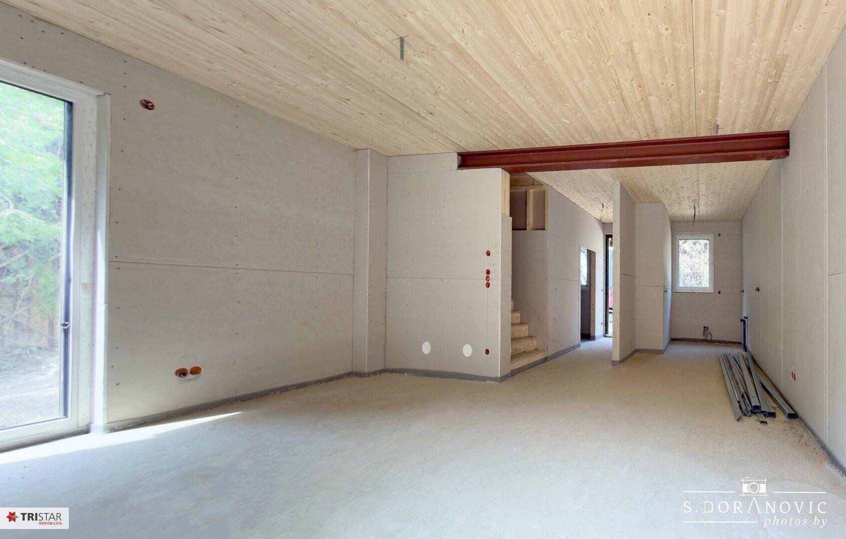 Heller Rohbau-Innenraum mit Holzdecken, Betonboden und sichtbarem Träger.