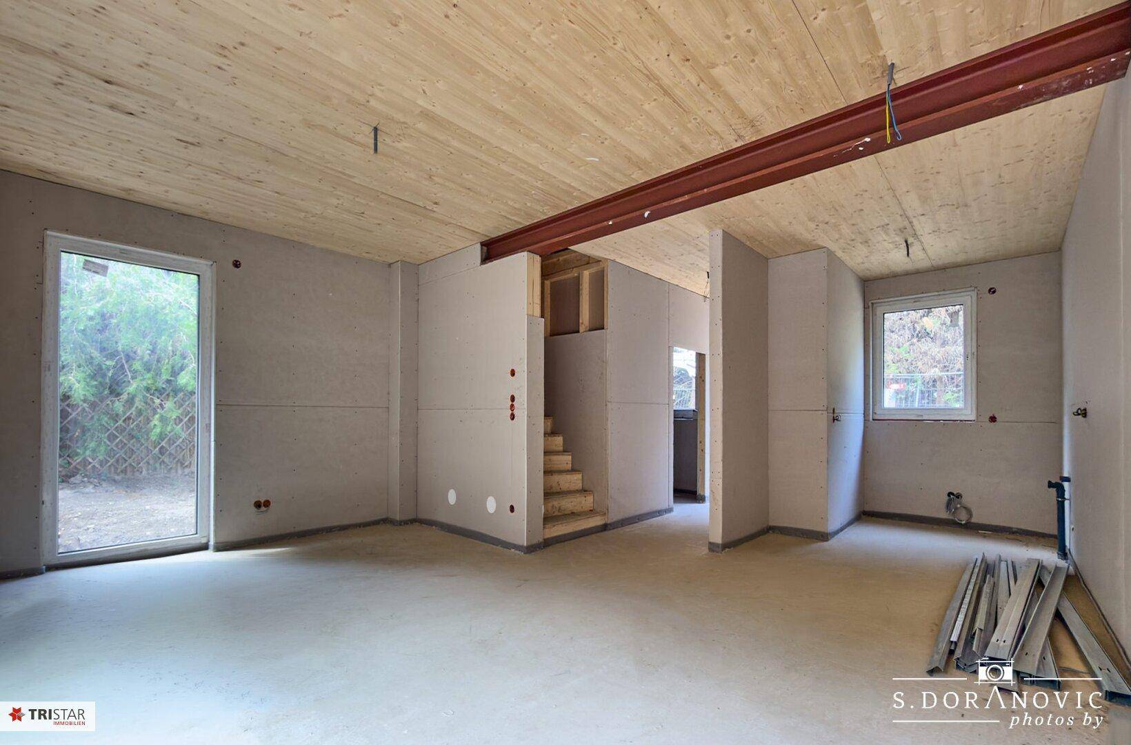 Unfertiger Innenraum mit Holzdecken, Betonboden und Treppenansatz, bereit für den weiteren Ausbau.