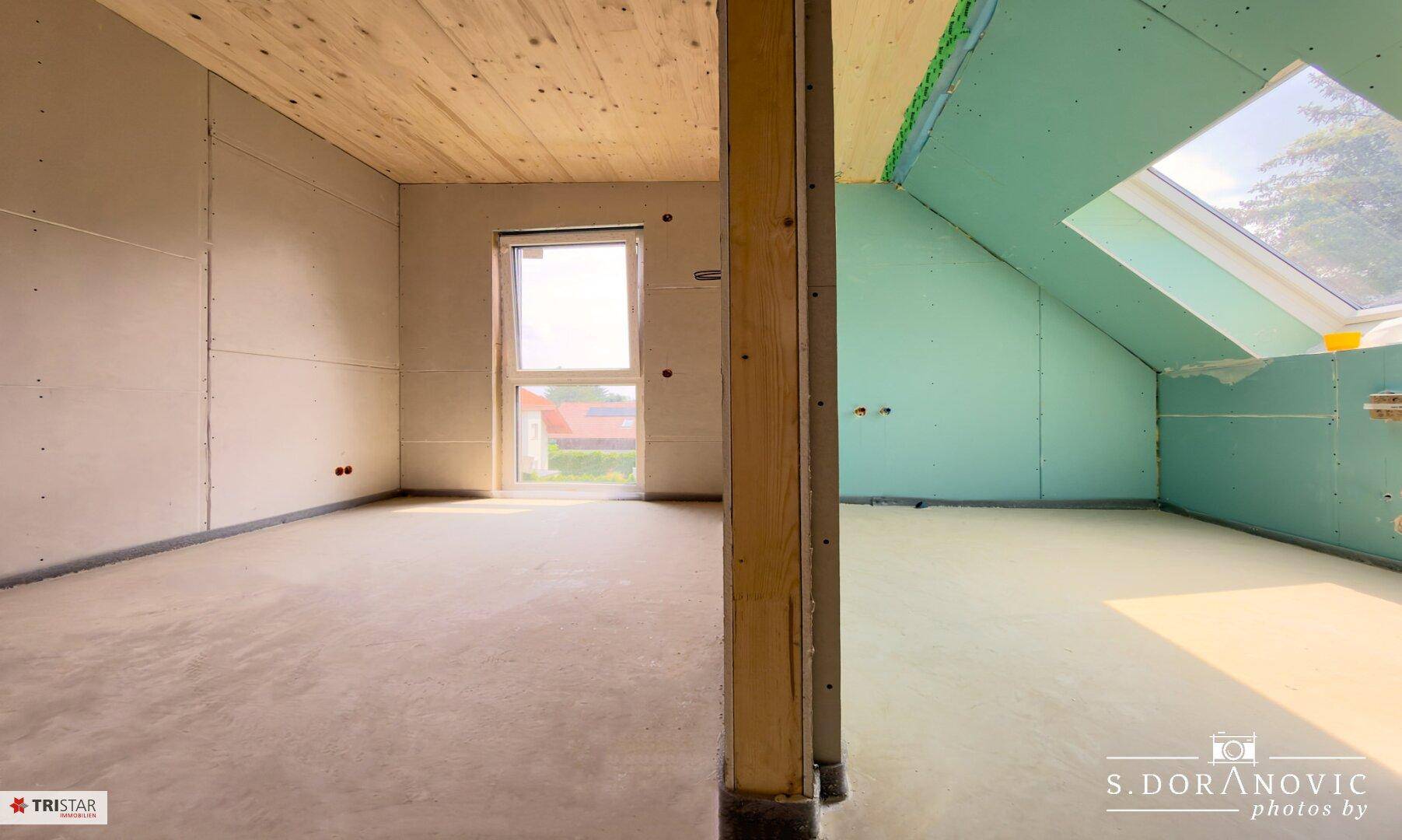 Unfertiger Dachgeschossraum mit schräger Decke, Betonboden und Dachfenster für natürliches Licht.