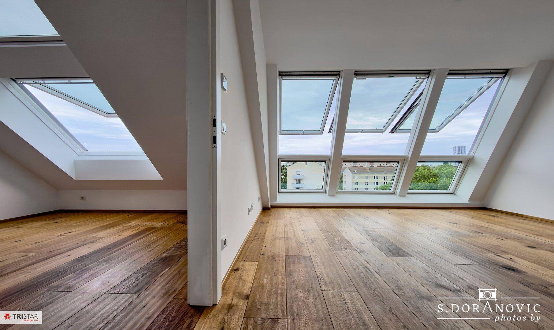Geräumiges Zimmer mit Holzboden und mehreren Dachfenstern, die eine helle und offene Atmosphäre schaffen.