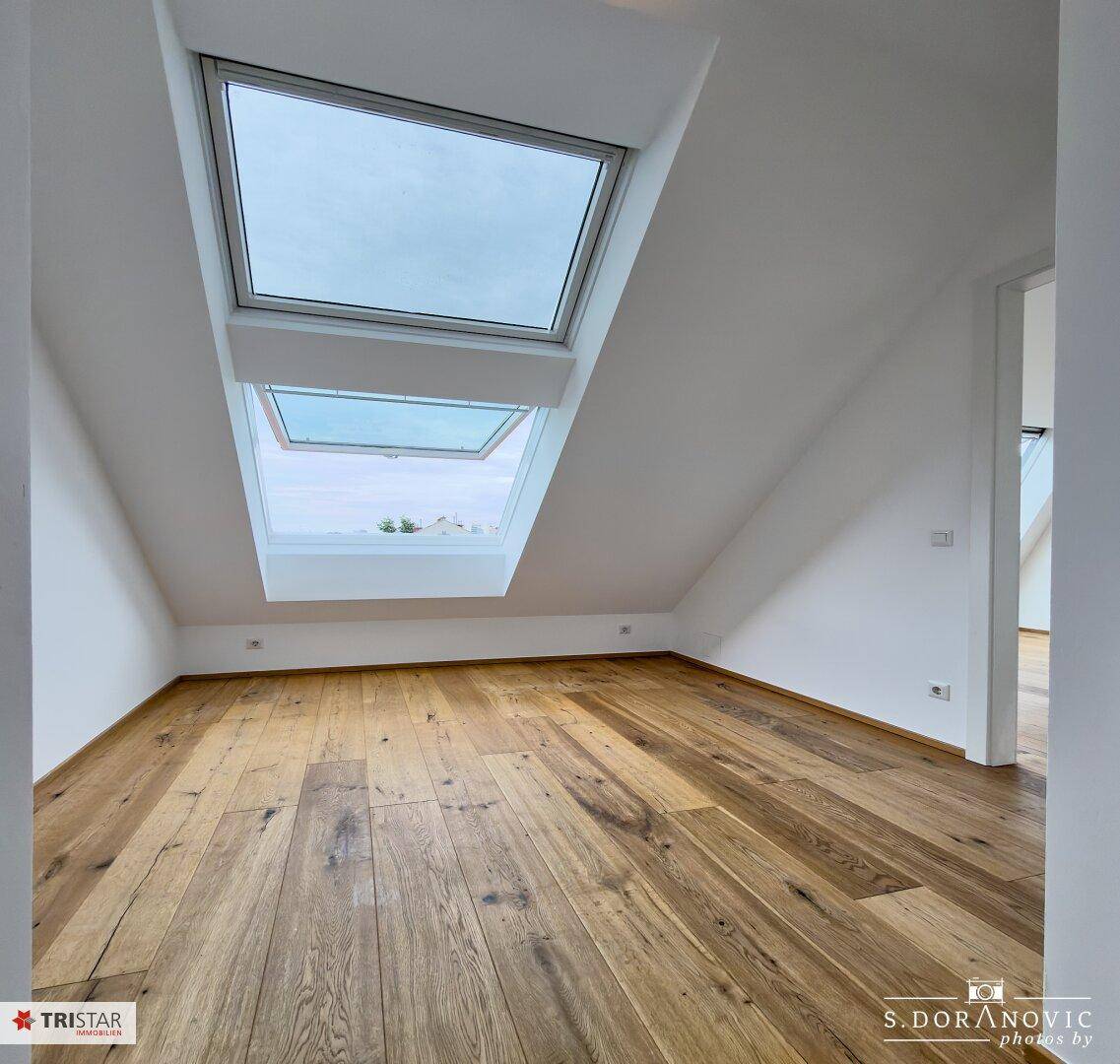 Heller Raum mit Holzboden und zwei großen Dachfenstern, die den Raum mit Tageslicht füllen.