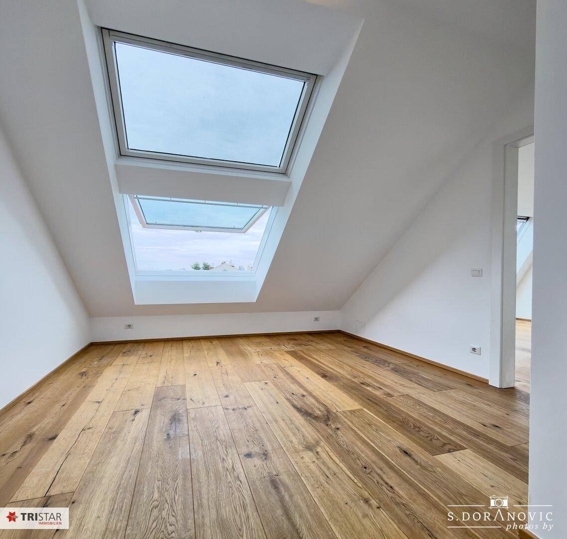 Heller Raum mit Holzboden und zwei großen Dachfenstern, die den Raum mit Tageslicht füllen.