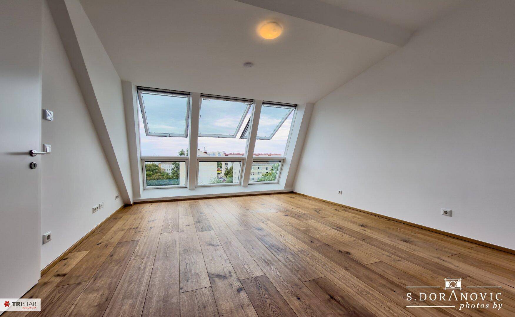 Geräumiges Zimmer mit Holzboden und großen Dachfenstern, die viel Licht hereinlassen.