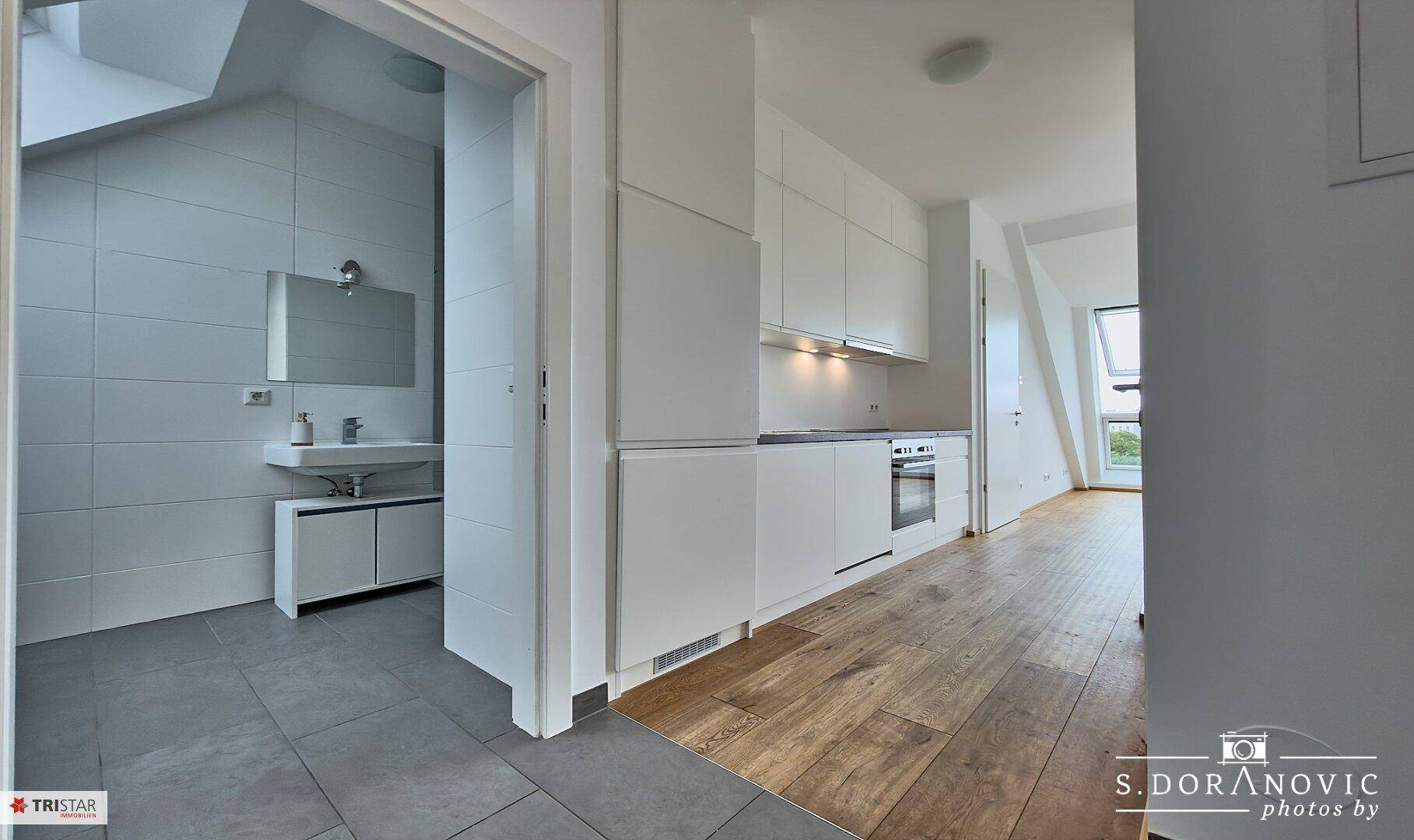 Offener Wohnbereich mit moderner Küche und Zugang zu einem gefliesten Badezimmer.