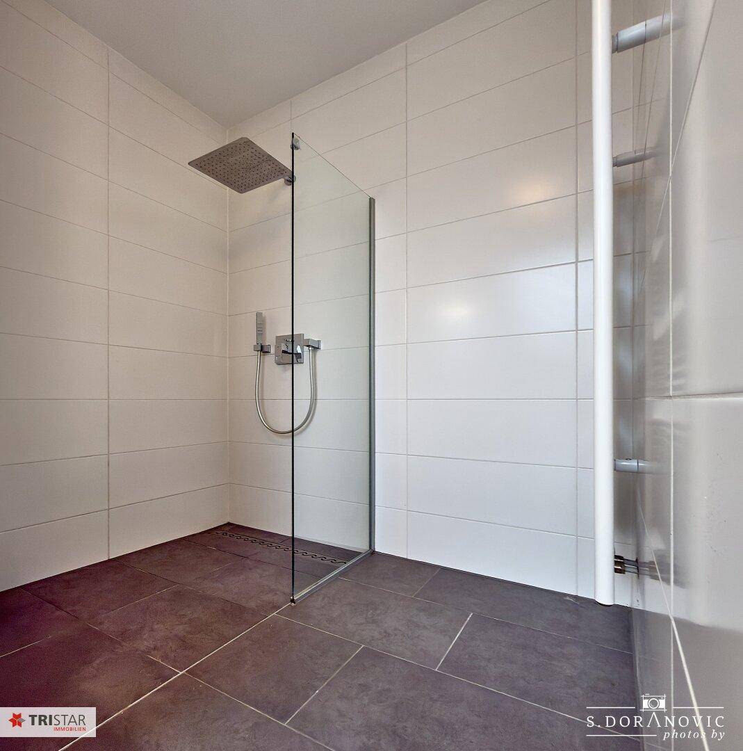Modernes Badezimmer mit großer begehbarer Dusche, Regendusche und beheiztem Handtuchhalter.