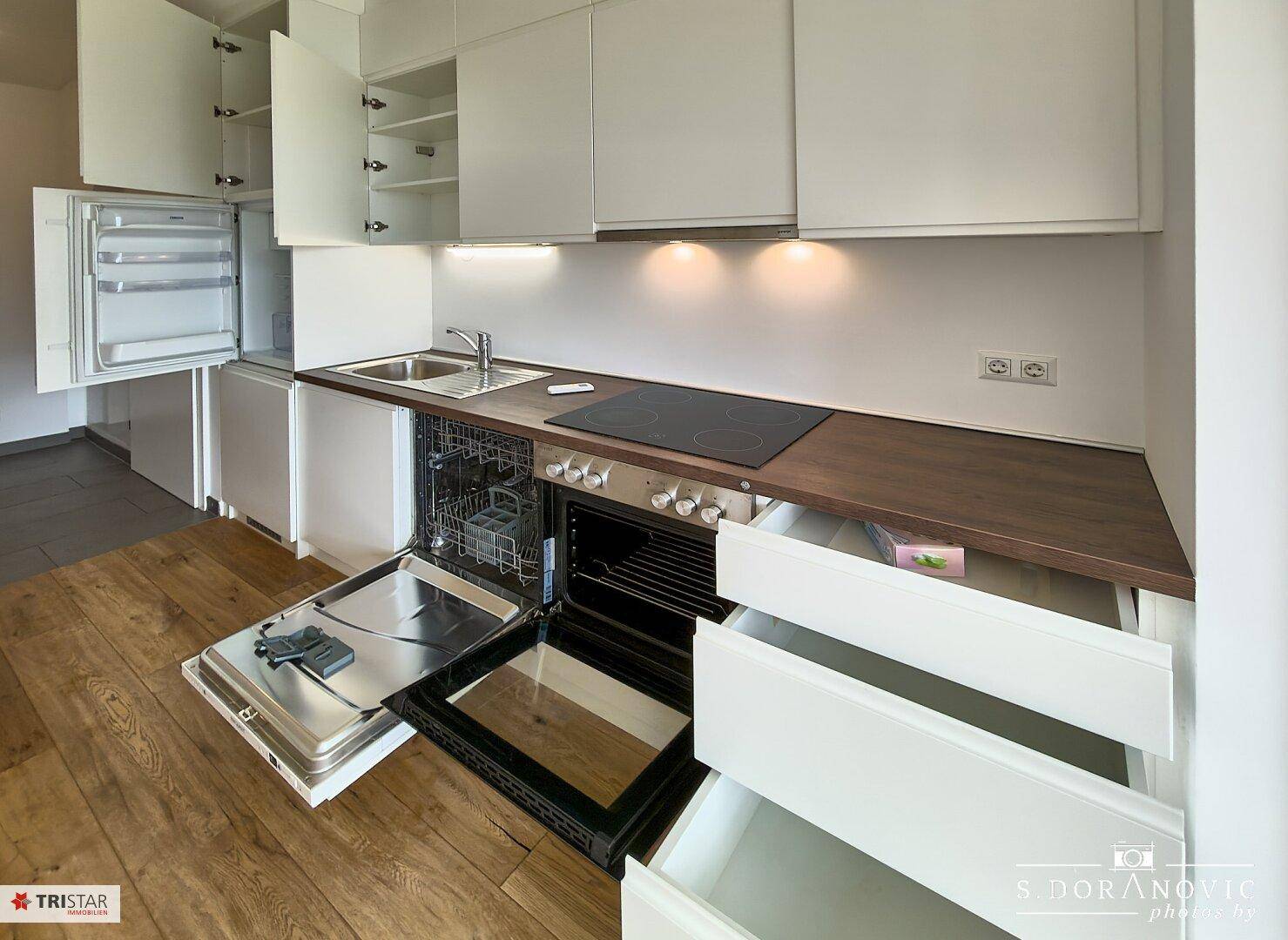 Voll ausgestattete moderne Küche mit geöffneten Schränken, Geschirrspüler und Backofen.