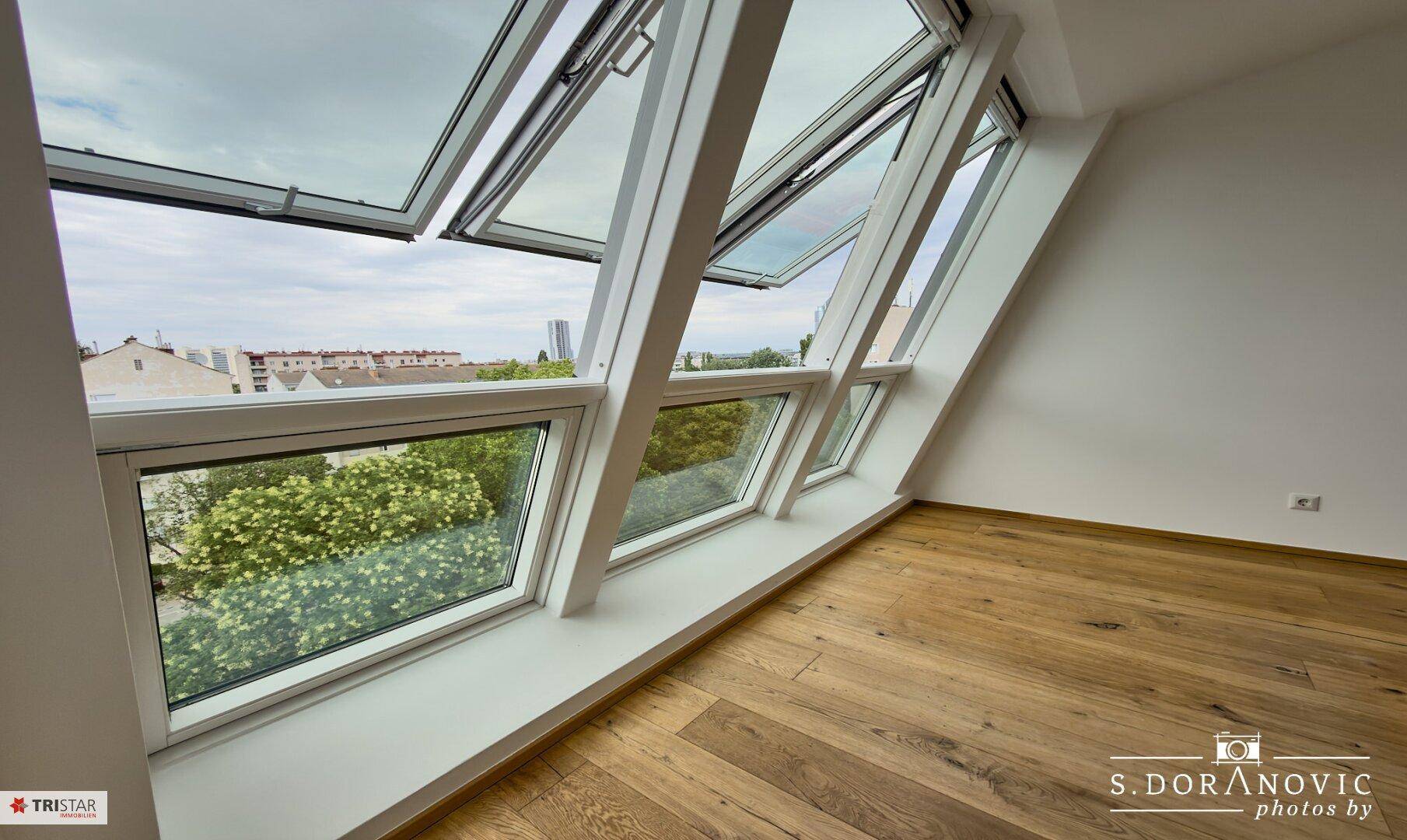 Helles Zimmer mit Holzboden und großen Dachfenstern, die einen weiten Blick nach draußen ermöglichen.
