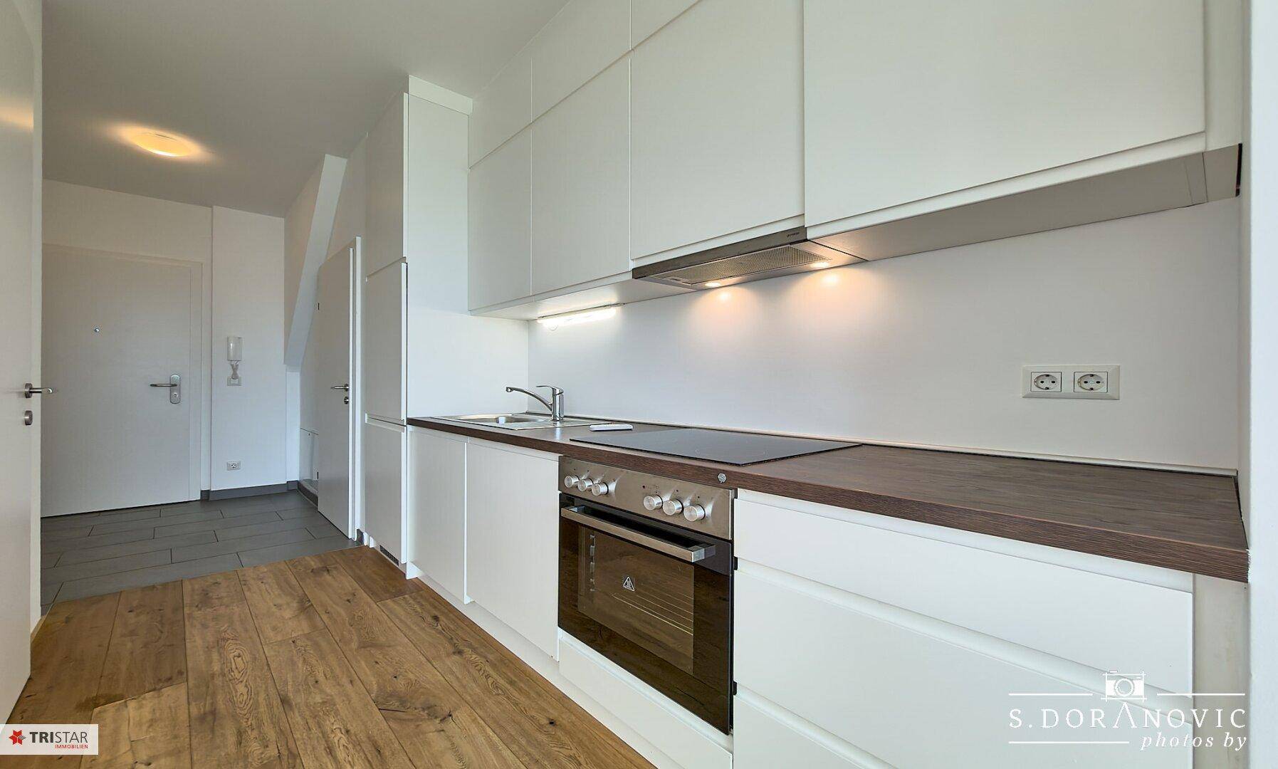 Moderne Einbauküche mit weißen Fronten, dunkler Arbeitsplatte und integrierten Geräten.