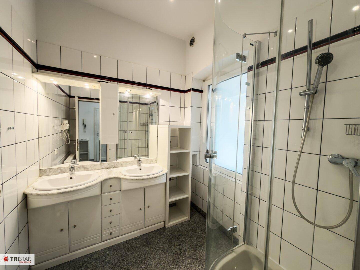 Badezimmer mit Doppelwaschbecken, weiß gefliesten Wänden und einer modernen Duschkabine.