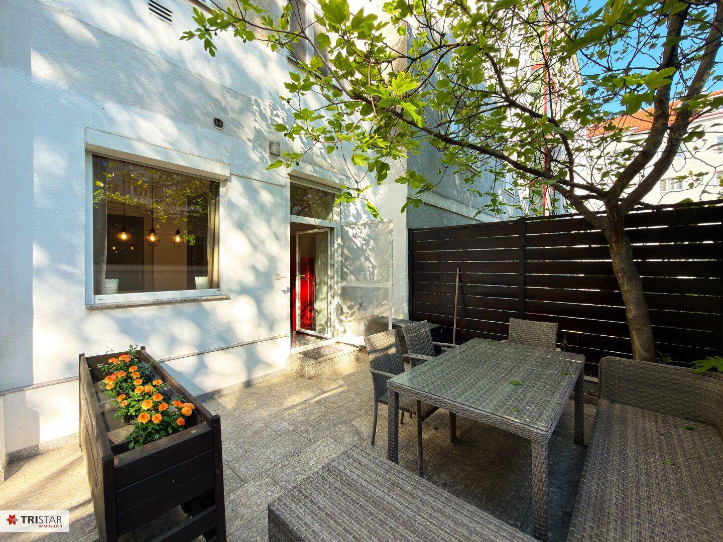 Gemütliche Terrasse mit Rattanmöbeln und einem Baum, ideal für entspannte Stunden im Freien.