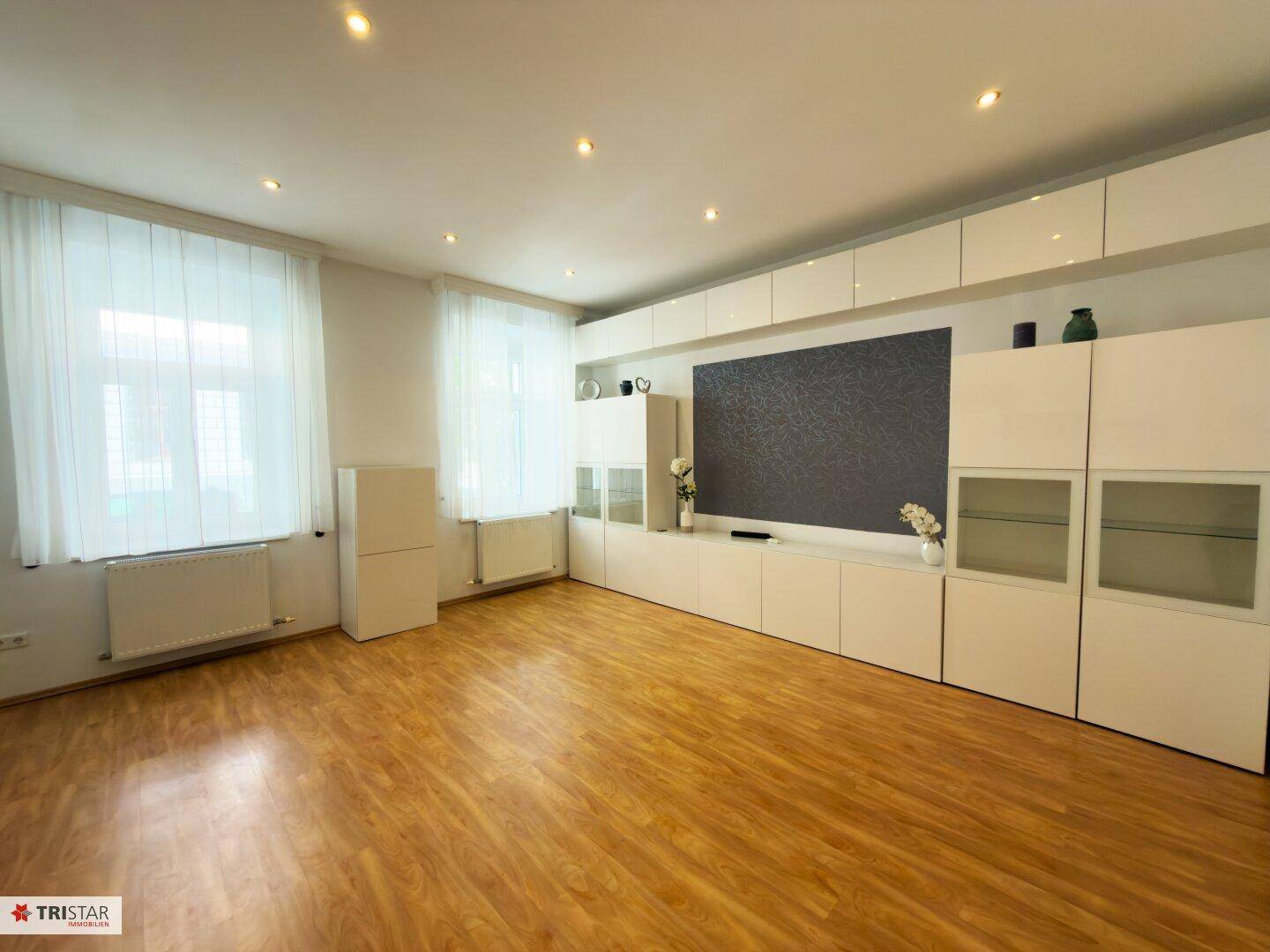 Helles Wohnzimmer mit Laminatboden und einer modernen, weißen Schrankwand.